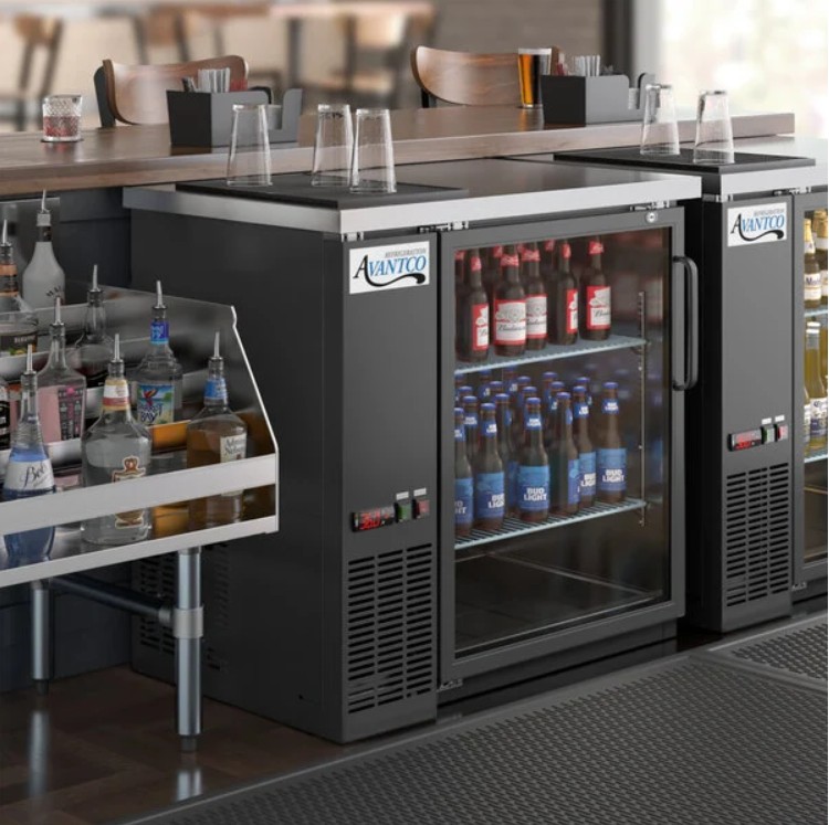 Avantco UBB-36G-HC 36-inch back bar cooler with glass door, shown under a bar counter stocked with beer bottles and spirits.